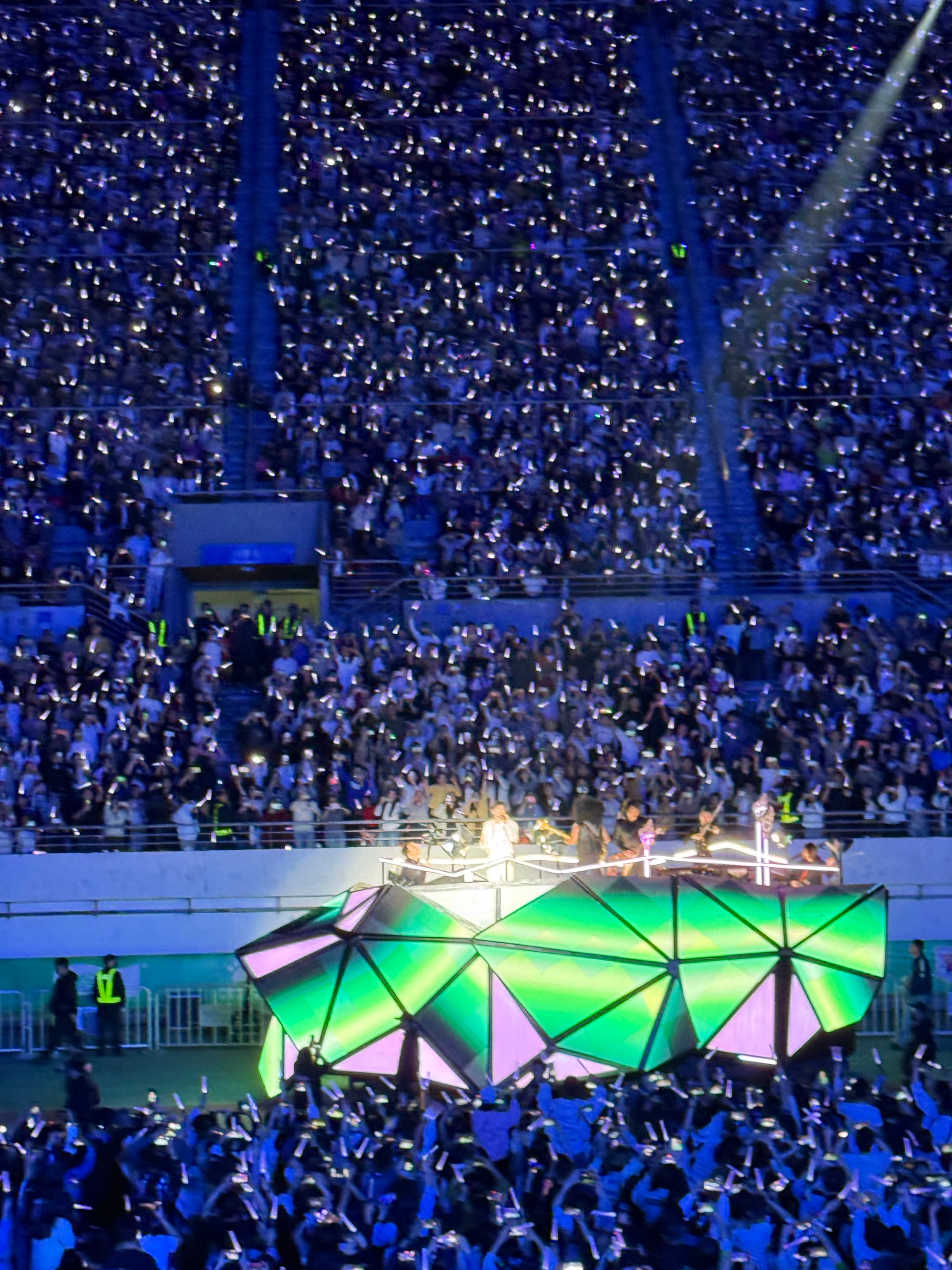 Acrylic light stick deploying glowing patterns over thousands of live music fans in a dark stadium crowd