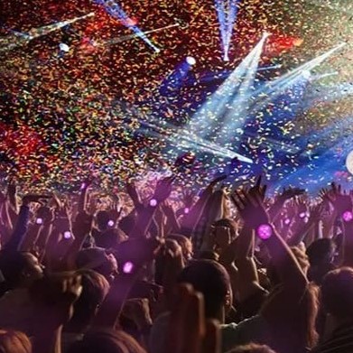 A sweeping wide shot of an arena crowd raising thousands of synchronized purple and cyan concert LED bracelets during an emotional acoustic solo