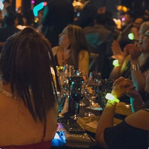 Indoor basketball arena filled with warm amber pulsing light from event bracelets worn by thousands of corporate attendees
