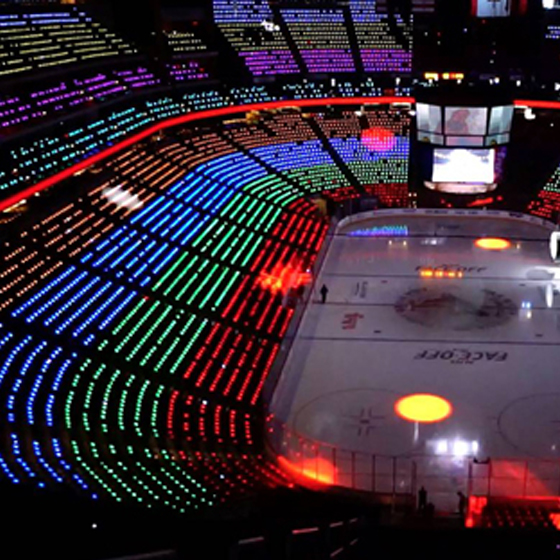 A high-altitude shot of a massive international arena concert completely lit by thousands of custom synchronized branding lightsticks
