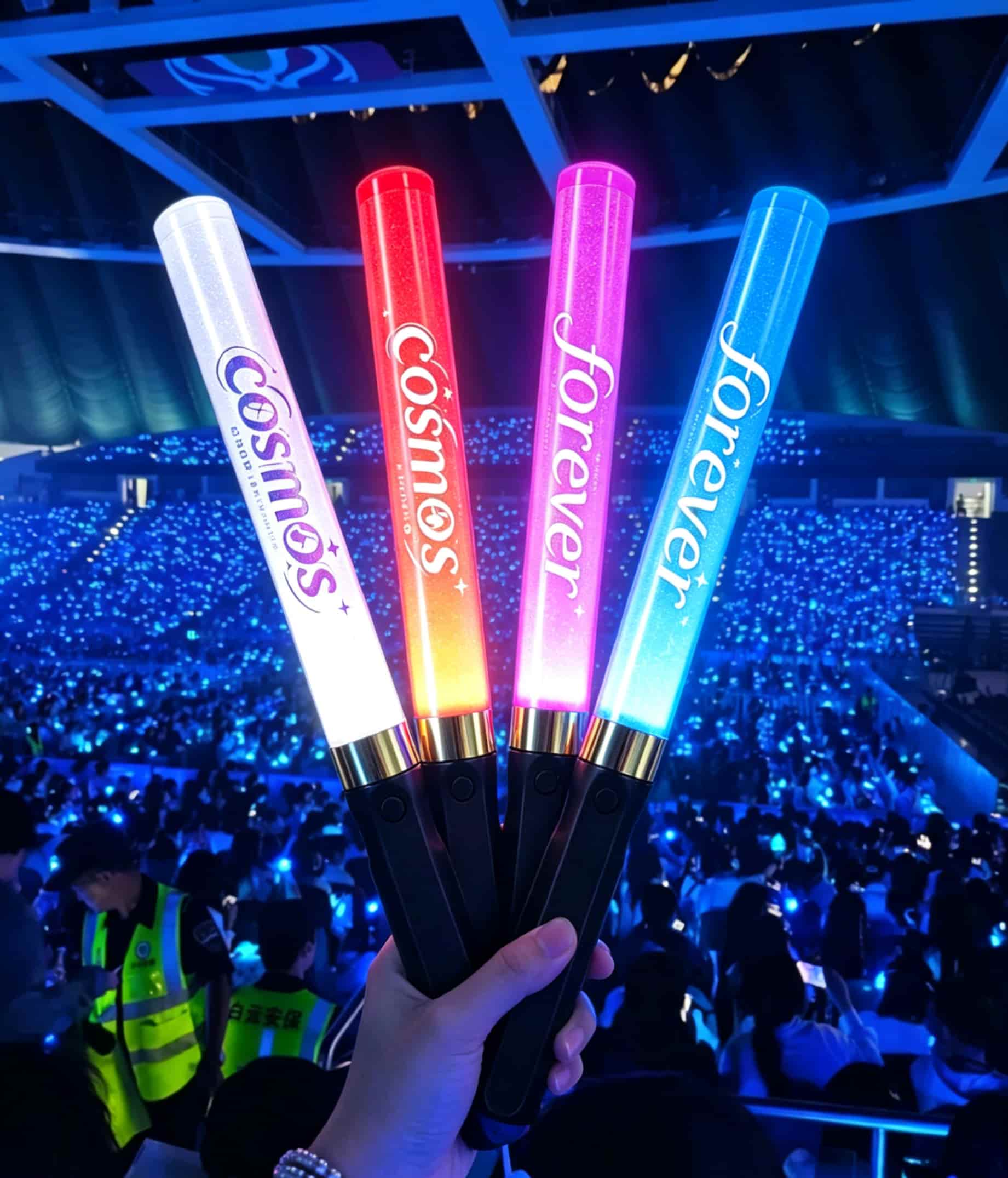 Massive crowd raising thousands of synchronized LED light sticks creating beautiful waves during a stadium concert show